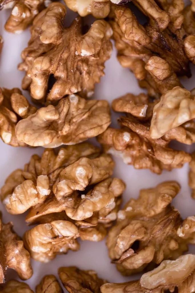 A close-up of golden-brown candied walnuts arranged on parchment paper, showing a glossy coating and light sprinkling of cinnamon.