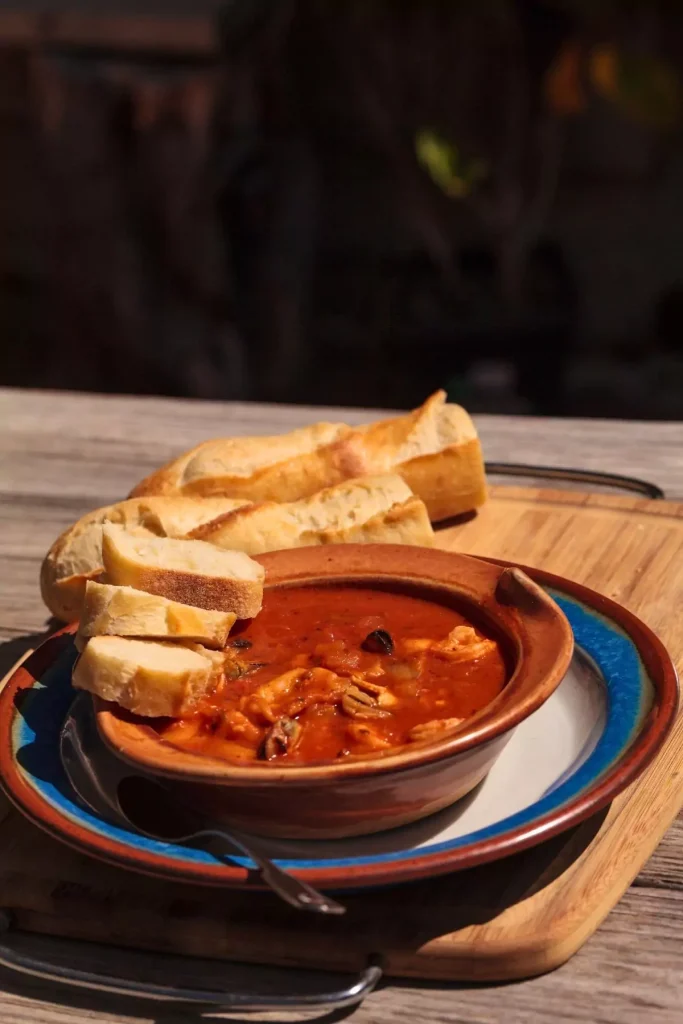 A bowl of Cioppino filled with fish, shrimp, clams, and crab in a tomato broth, garnished with fresh parsley and served with crusty bread.