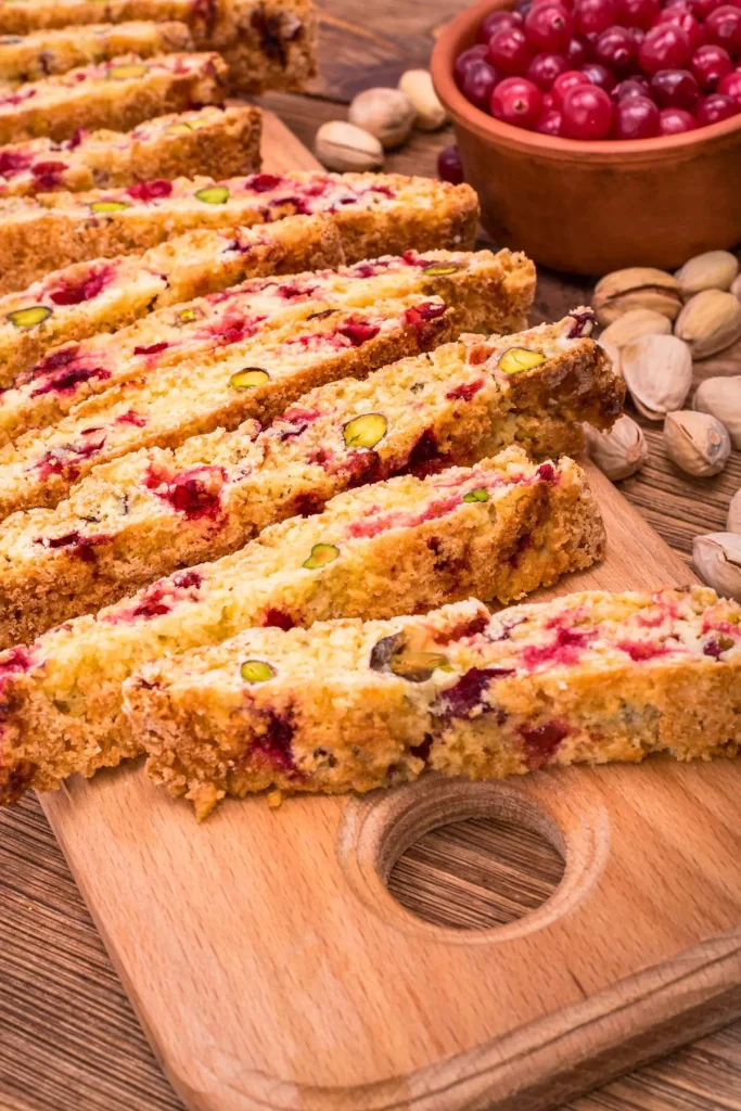 Cranberry Pistachio Biscotti on a cutting board sheet, showing their golden brown edges with visible chunks of dried cranberries and pistachios.