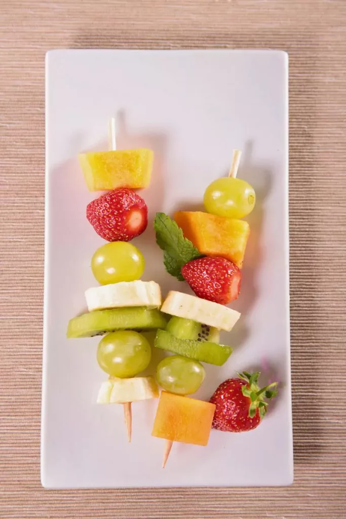 A plate of festive Grinch Kabobs made with green grapes, banana slices, strawberries, and marshmallows, perfect for a holiday appetizer.