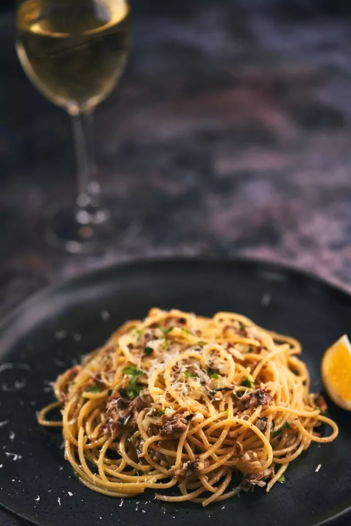 A plate of Sicilian Anchovy Pasta topped with breadcrumbs and parsley, served with grated Parmesan.