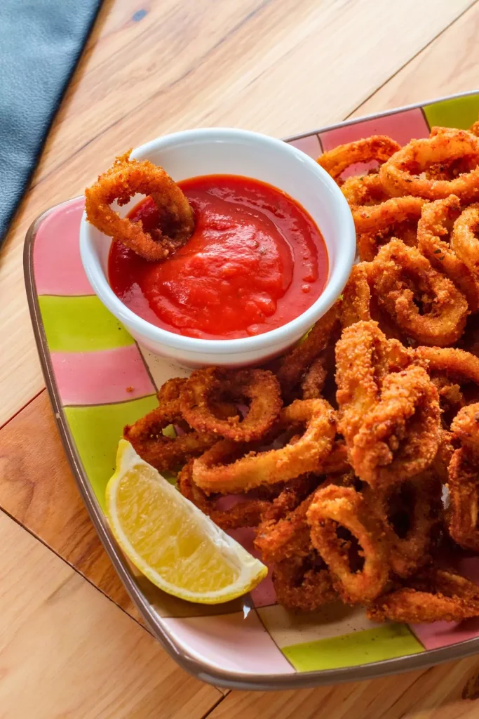 A close-up view of calamari rings simmered in tomato sauce, served over linguine on a plate.