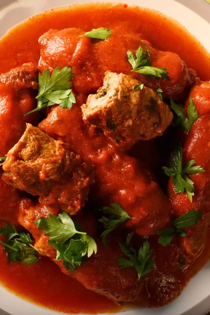 A plate of sliced braciole served over spaghetti, topped with rich tomato sauce, grated Parmesan, and fresh parsley.