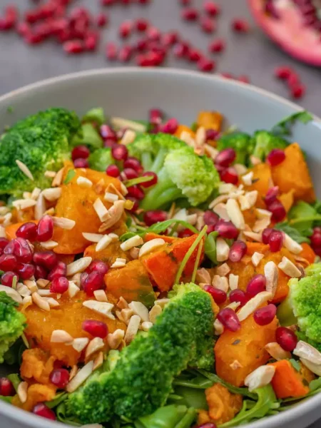 A festive Christmas pomegranate salad in a large bowl with leafy greens, pomegranate seeds, crumbled blue cheese, and walnuts, ready to serve.