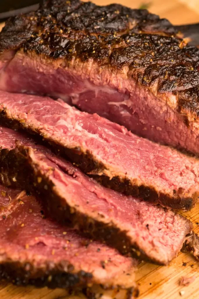 Sliced prime rib with a golden crust served on a wooden board, surrounded by roasted vegetables and a bowl of au jus.