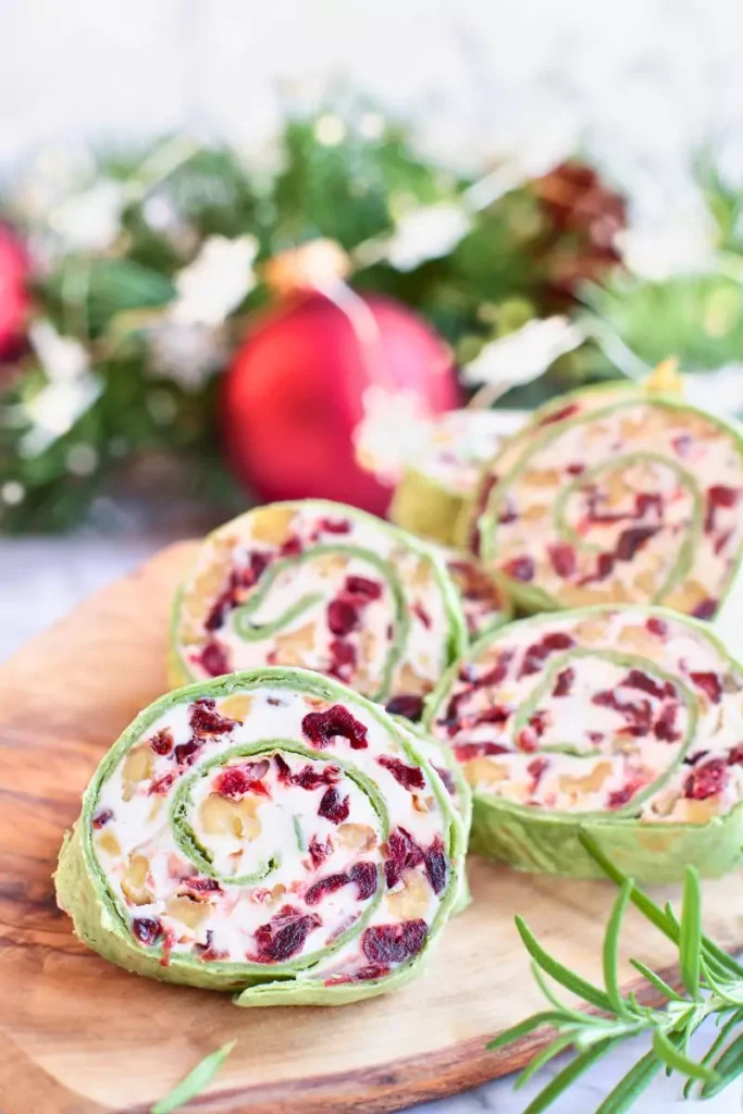 A plate of festive Christmas pinwheel appetizers featuring cream cheese, diced red peppers, celery, green onions, and olives rolled in tortillas and arranged beautifully.