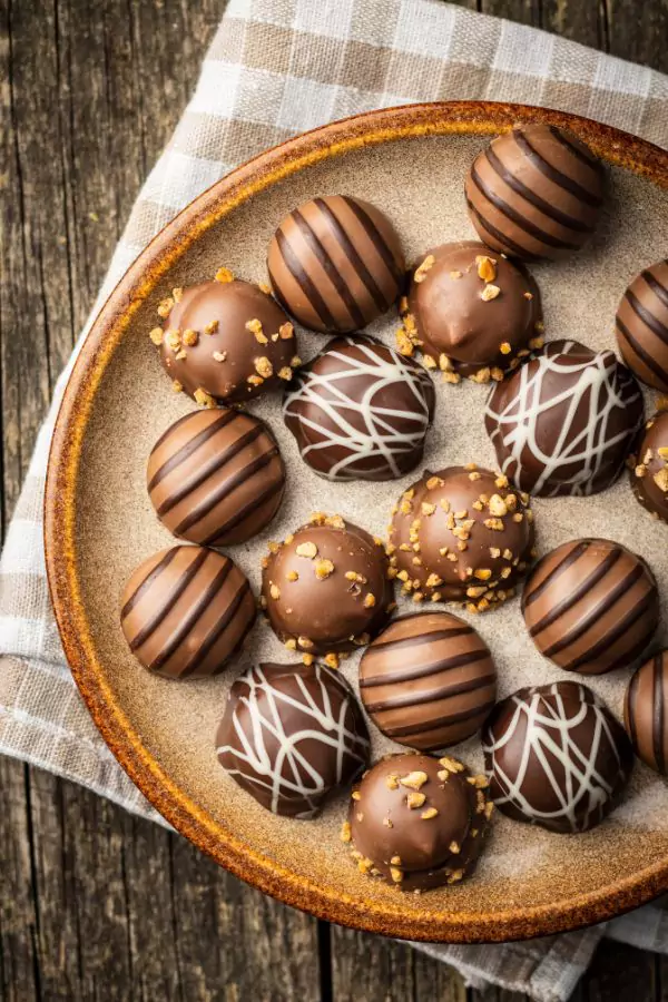 A close-up view of Coconut Bonbons coated in chocolate and set on a wooden platter, perfect for Christmas celebrations.