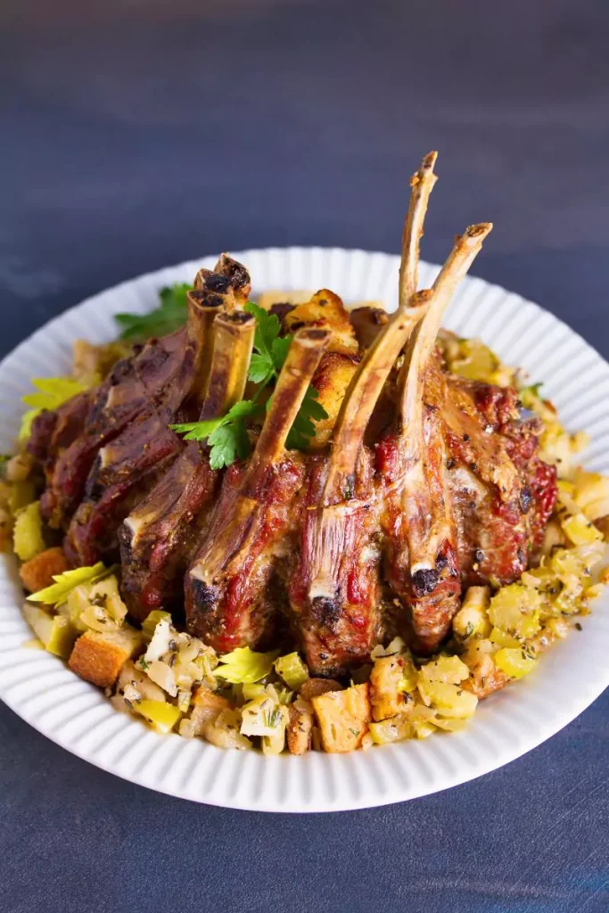 A golden-brown crown roast of pork garnished with cranberries and mushroom dressing, served on a decorative platter.