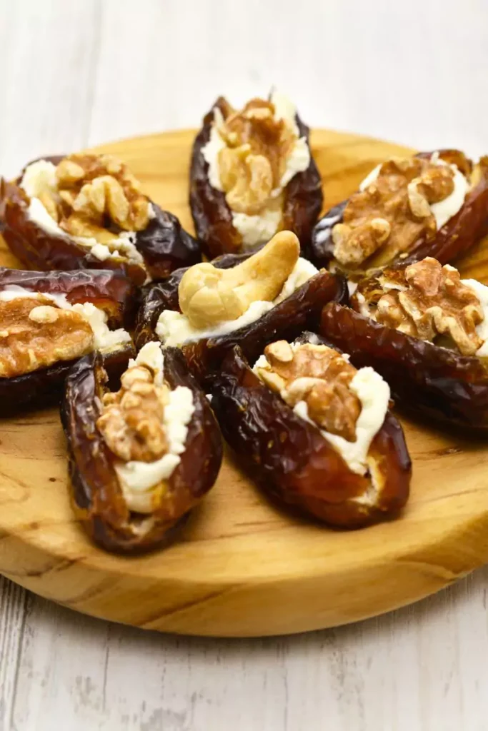 Close-up of stuffed dates filled with creamy Gorgonzola and topped with walnut pieces on a serving platter.