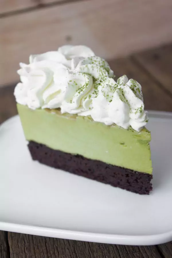 A slice of grasshopper pie with a chocolate cookie crust and minty green filling, topped with white cream.