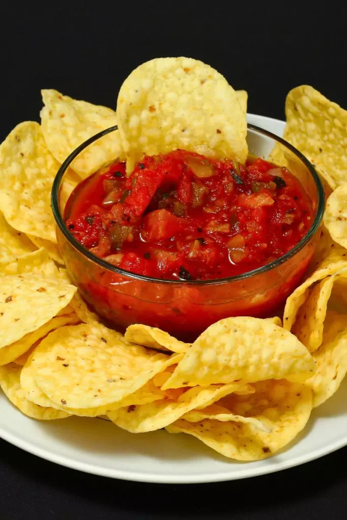 A festive serving of Holiday Salsa with cranberries, green onions, and cilantro over cream cheese, accompanied by crackers and tortilla chips on a holiday-themed plate.