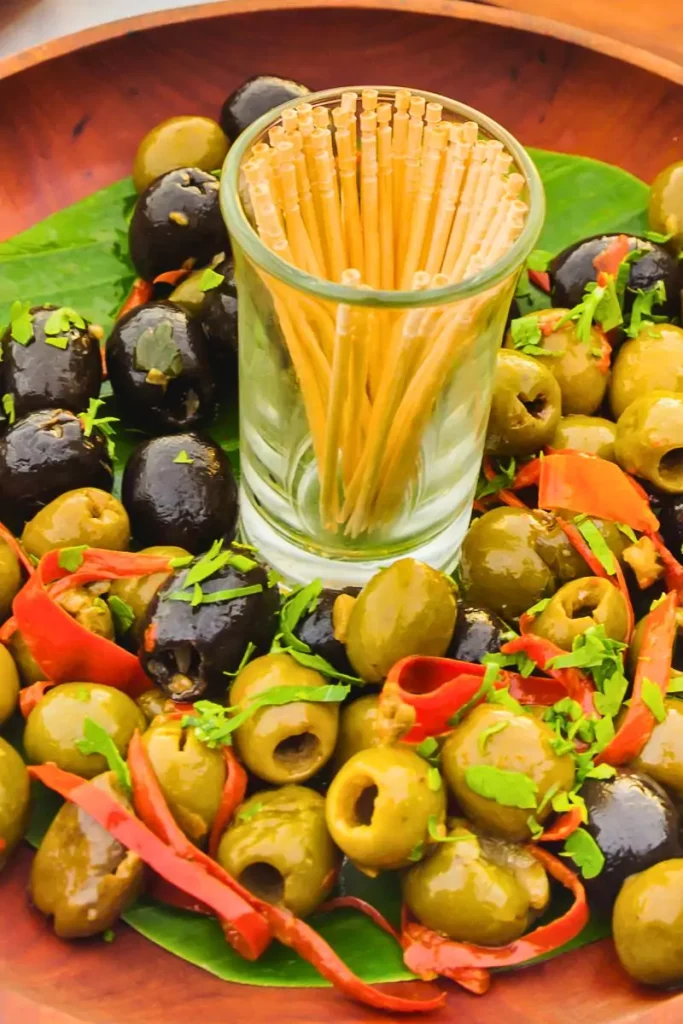 A bowl of Italian marinated olives garnished with herbs and spices, showcasing a mix of black and green olives with vibrant colors perfect for an antipasto spread.