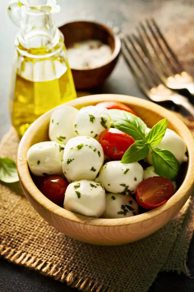 Close-up of marinated mozzarella cubes with herbs, red pepper flakes, and sun-dried tomatoes in a bowl.