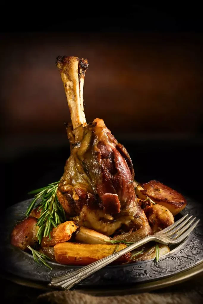 A beautifully roasted lamb leg with a shiny plum glaze, garnished with fresh herbs.