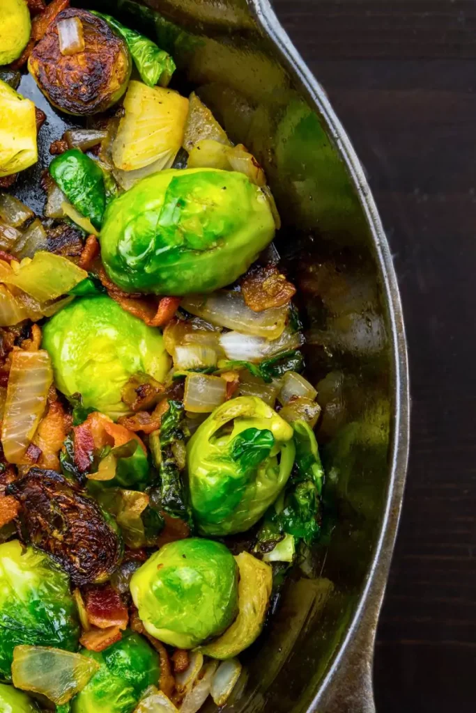 A serving of roasted acorn squash and Brussels sprouts topped with toasted pecans and maple syrup, arranged on a rustic white plate