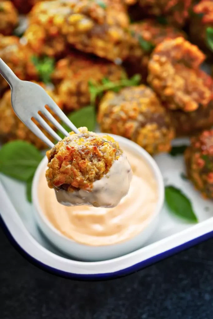 A close-up of golden-brown sausage cheese balls on a plate with barbecue and sweet-and-sour sauces for dipping.