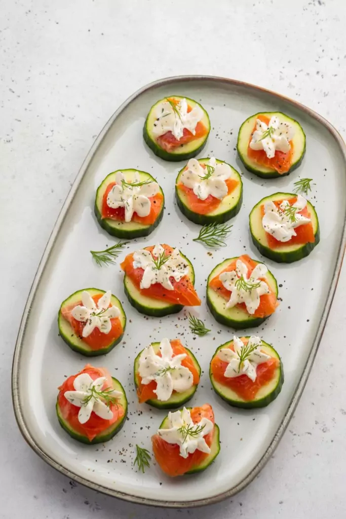 Close-up of Smoked Salmon Bites on a platter, featuring radish or cracker base, creamy yogurt, smoked salmon, and garnishes of capers and red onion.