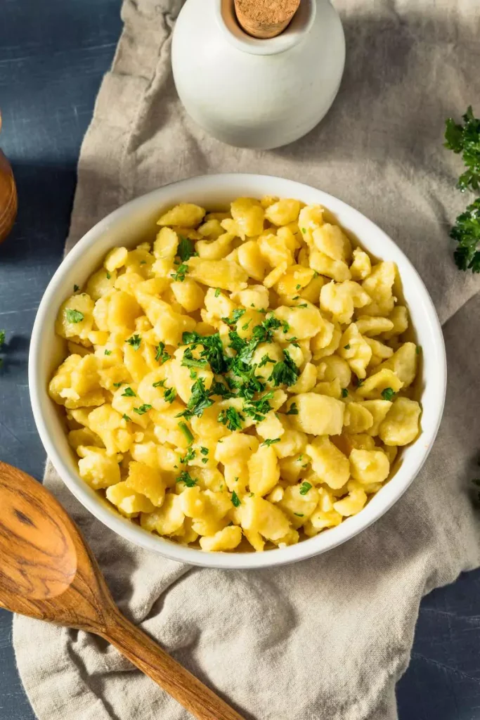 A plate of homemade spaetzle dumplings garnished with fresh parsley, served in a rustic, comforting style