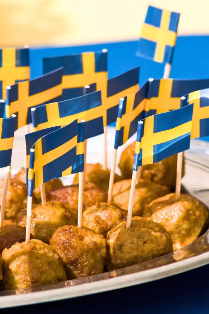 A close-up of traditional Swedish meatballs on a plate with small flags of Sweden on them