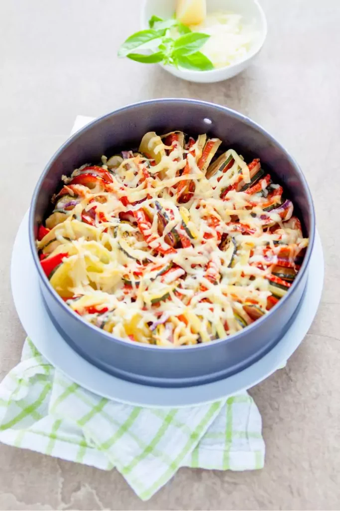 A vibrant Vegetable Tian in a cast-iron skillet, layered with colorful slices of zucchini, tomatoes, potatoes, and butternut squash, topped with melted Gruyere cheese and crispy bread crumbs.