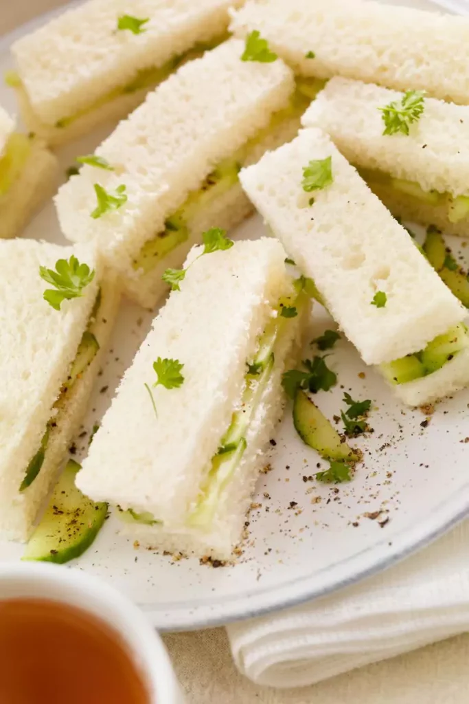 A close-up of cucumber sandwiches with a creamy spread on rye bread, topped with fresh cucumber slices and garnished with dill.