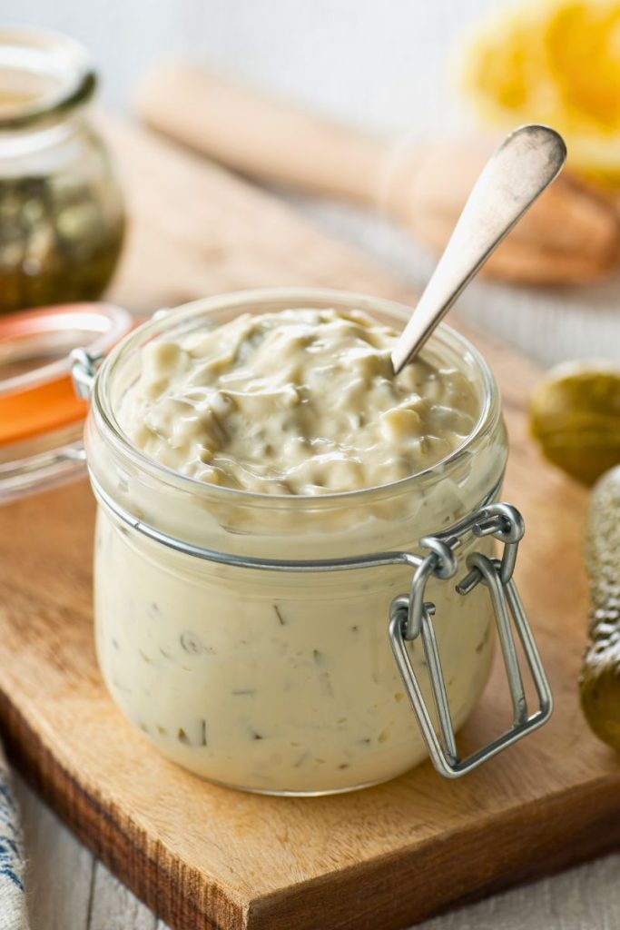 A bowl of creamy dill pickle dip served with potato chips and garnished with fresh dill