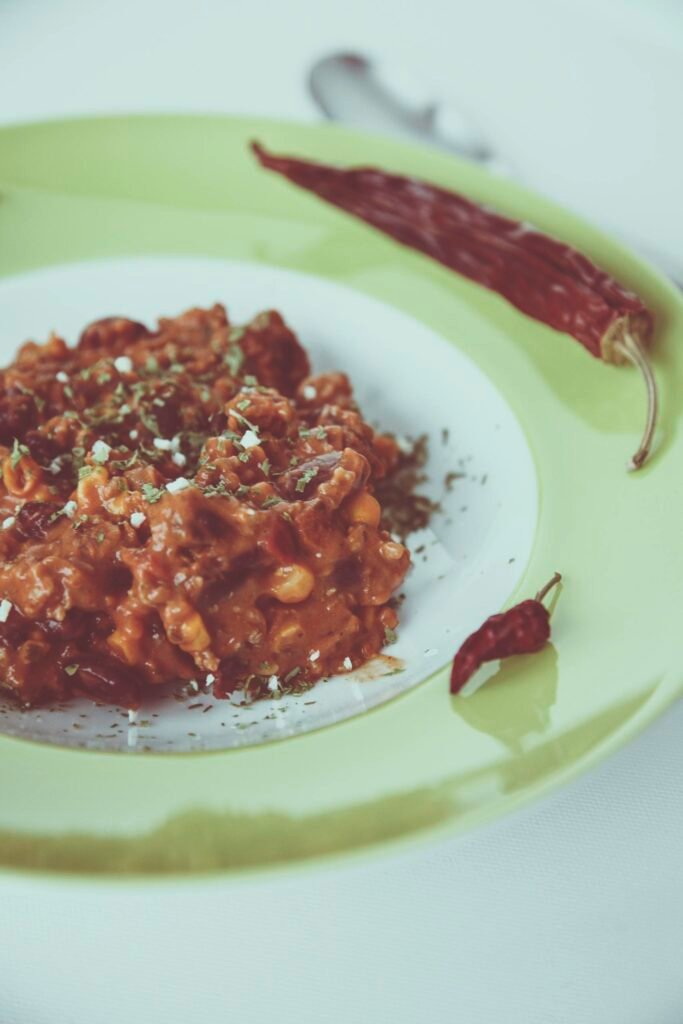 Delicious chili dish served with red chili peppers garnished on a green plate.